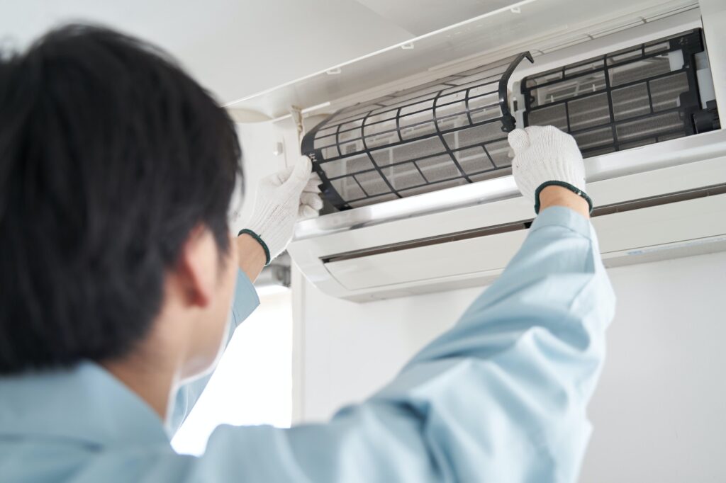 A Japanese male electrician checking a home air conditioner's filters
