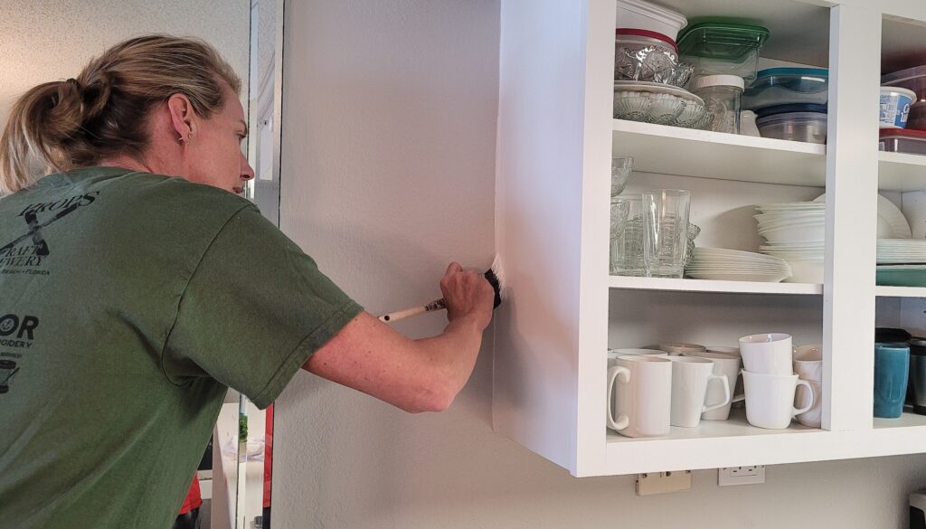 Business woman in work clothes applying second coat of paint to kitchen cabinets with care.