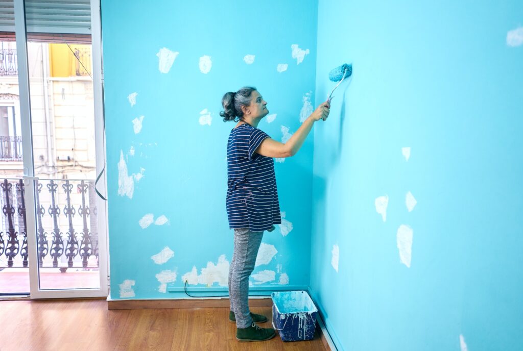 happy woman painting interior wall with paint roller in new house