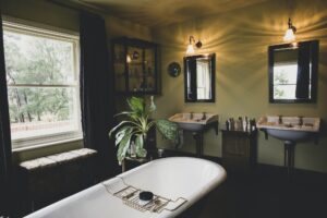 Interior view of bathroom with black mirrors over two Victorian wash stands, sash window and roll