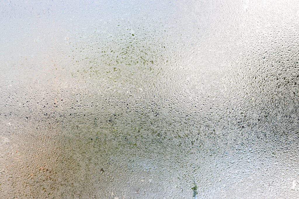 Misted glass, silver rain drops dew drops on transparent glass window.