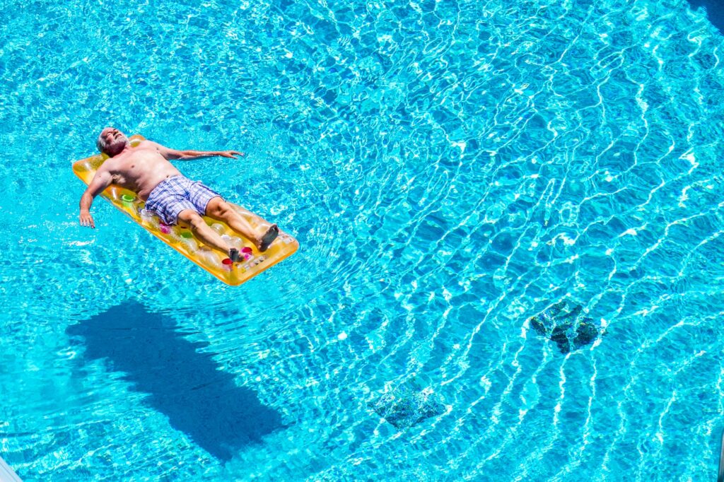 Senior aged man sleep and relax enjoying the blue water of swimming pool lay down on lilo