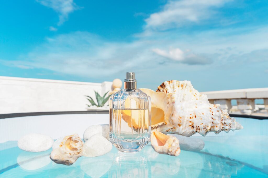 transparent spray bottle of women's or men's perfume with shells on the glass surface of the pool